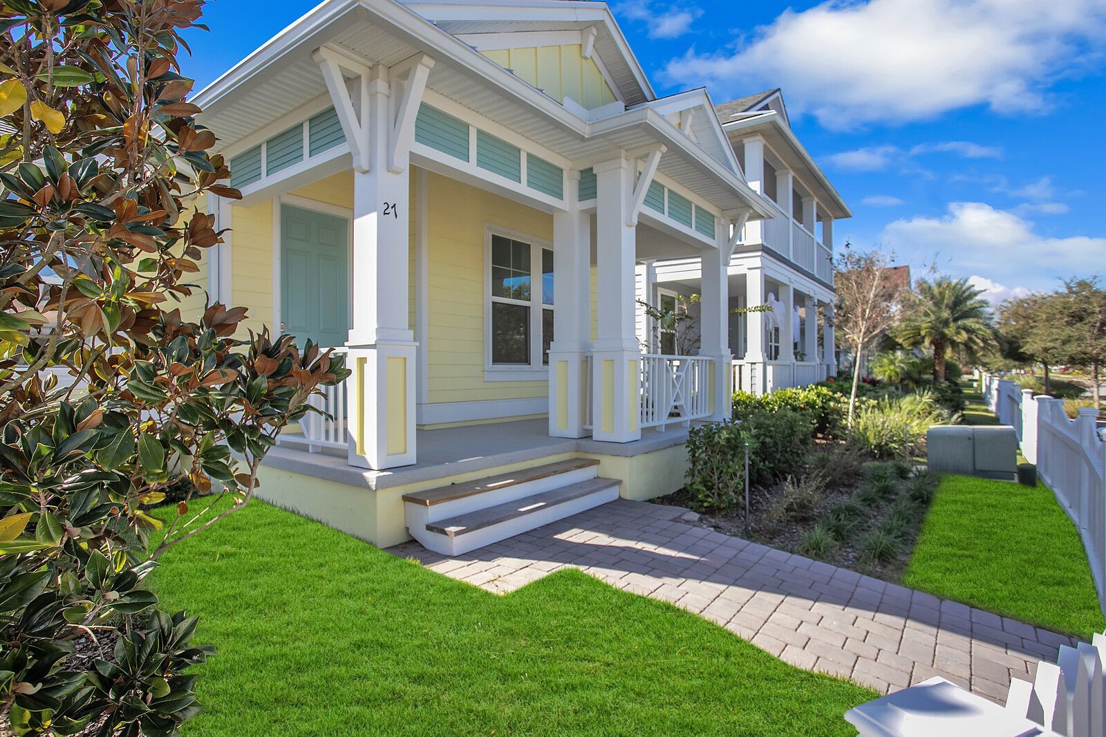 A yellow and white house with a porch and a brick walkway.