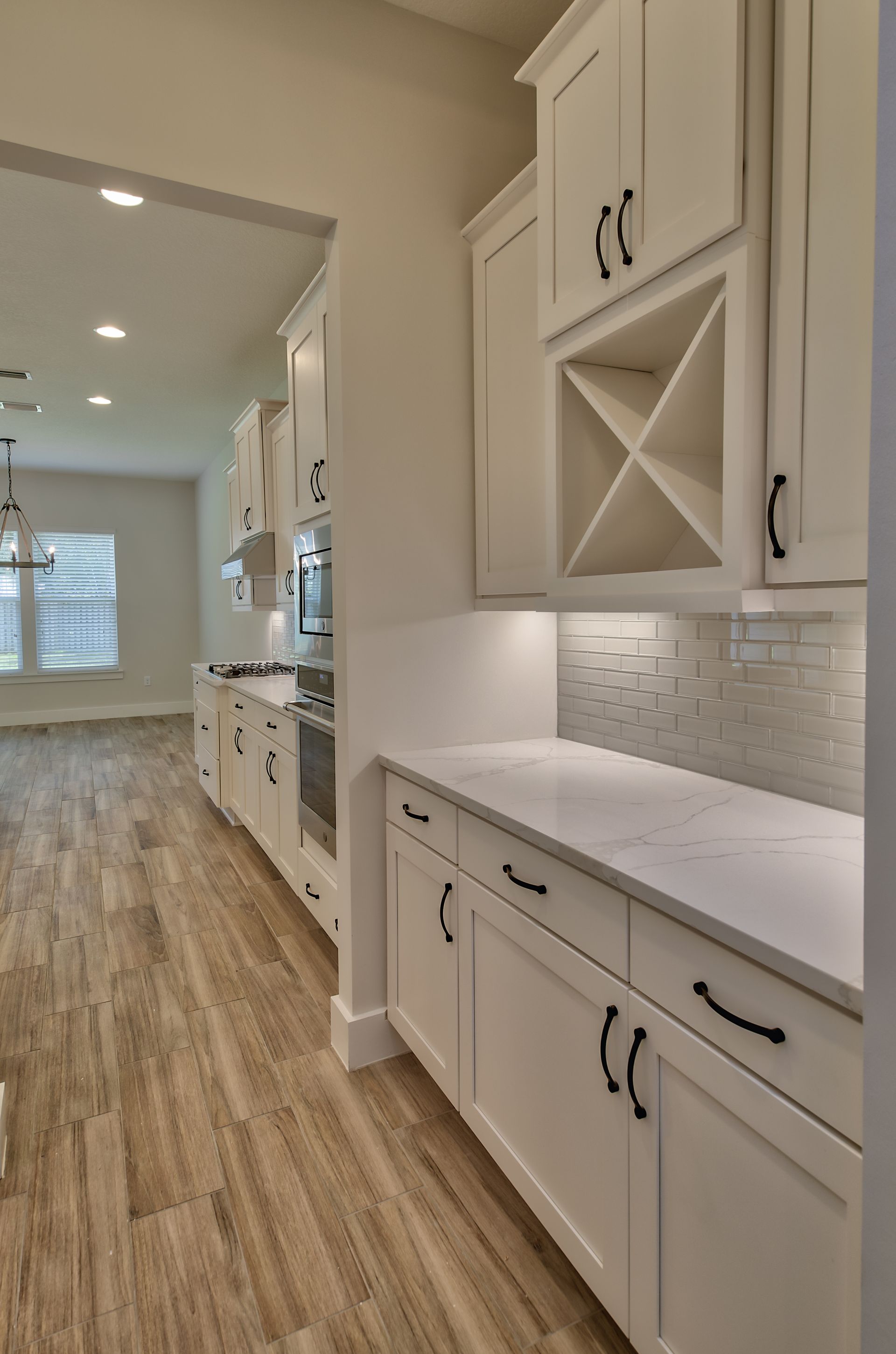 A kitchen with white cabinets and wooden floors and a wine rack.