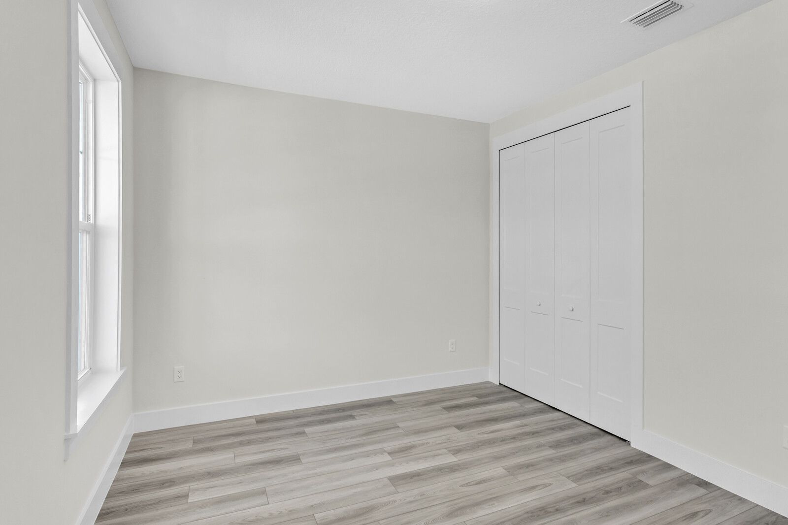 An empty bedroom with hardwood floors and white walls.