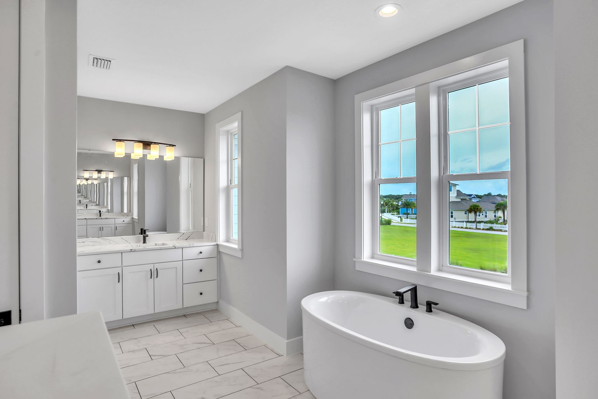 A bathroom with two sinks , a tub , and two windows.