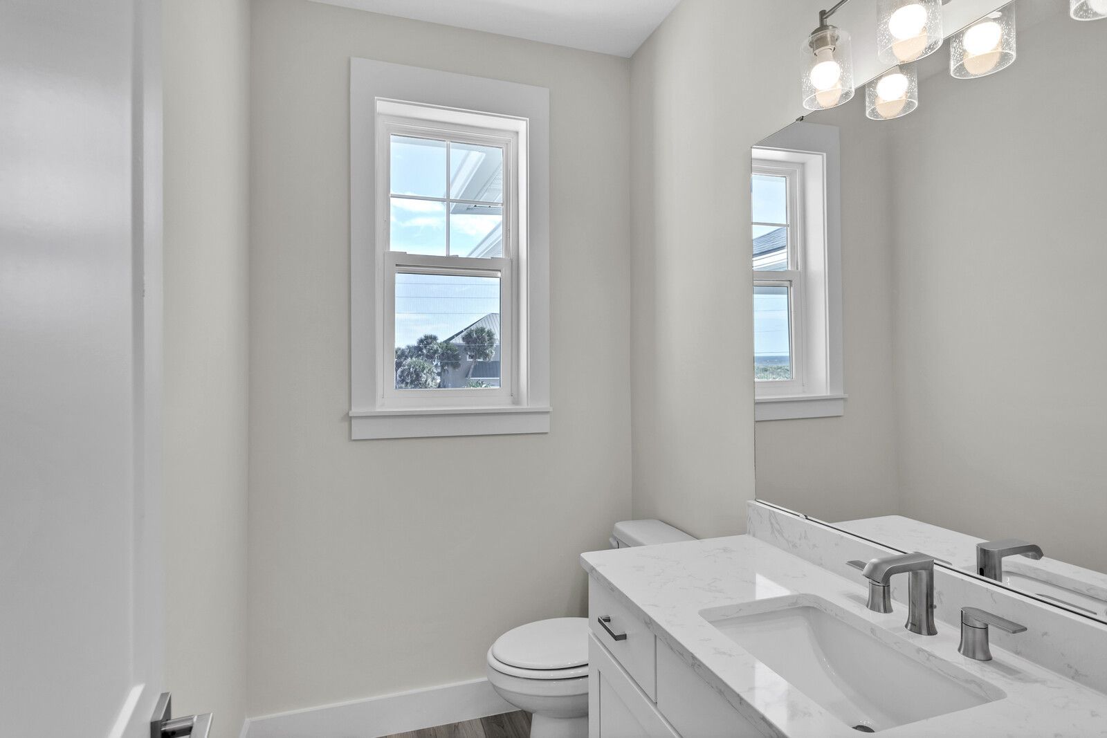 A bathroom with a toilet , sink , mirror and window.