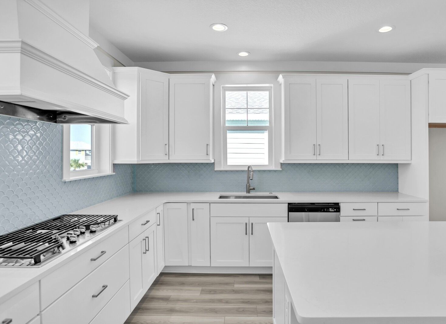 A kitchen with white cabinets , a stove , a sink , and a window.