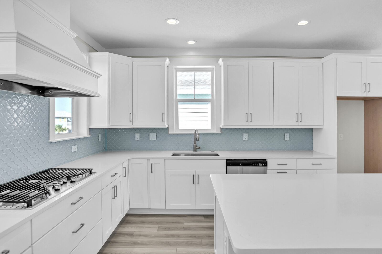 A kitchen with white cabinets , a stove , a sink , and a window.