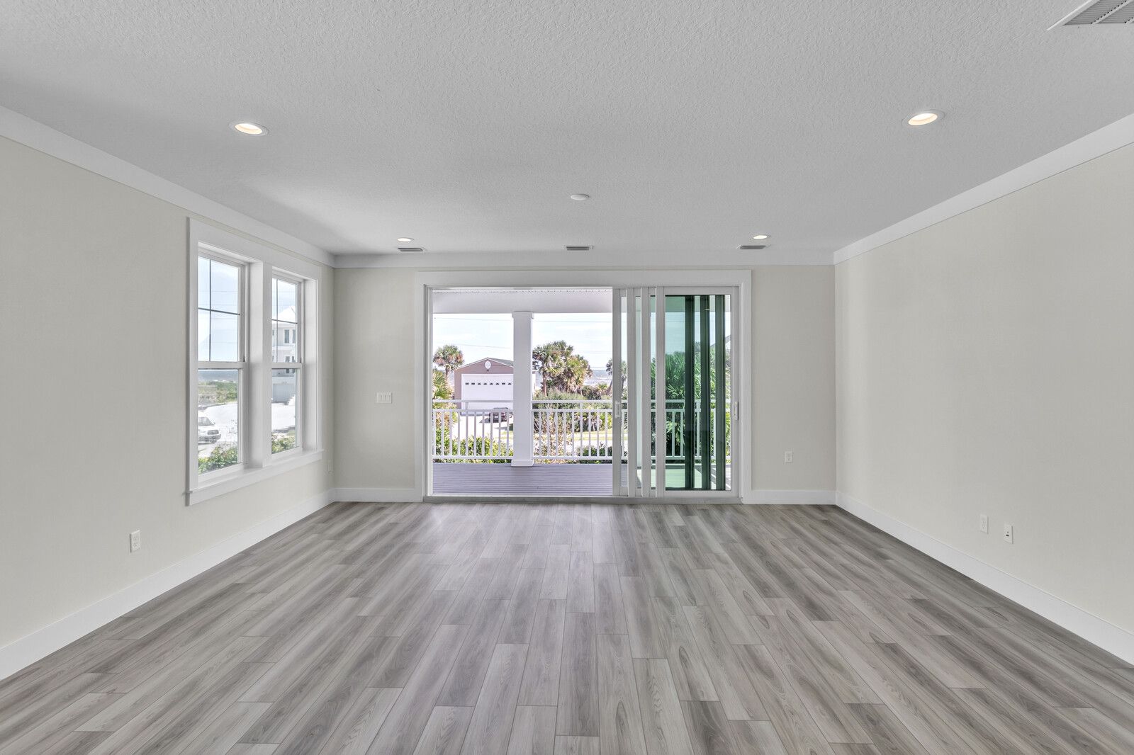 An empty living room with hardwood floors and sliding glass doors.