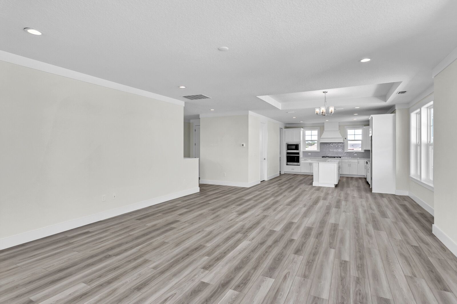 An empty living room with hardwood floors and a kitchen in the background.