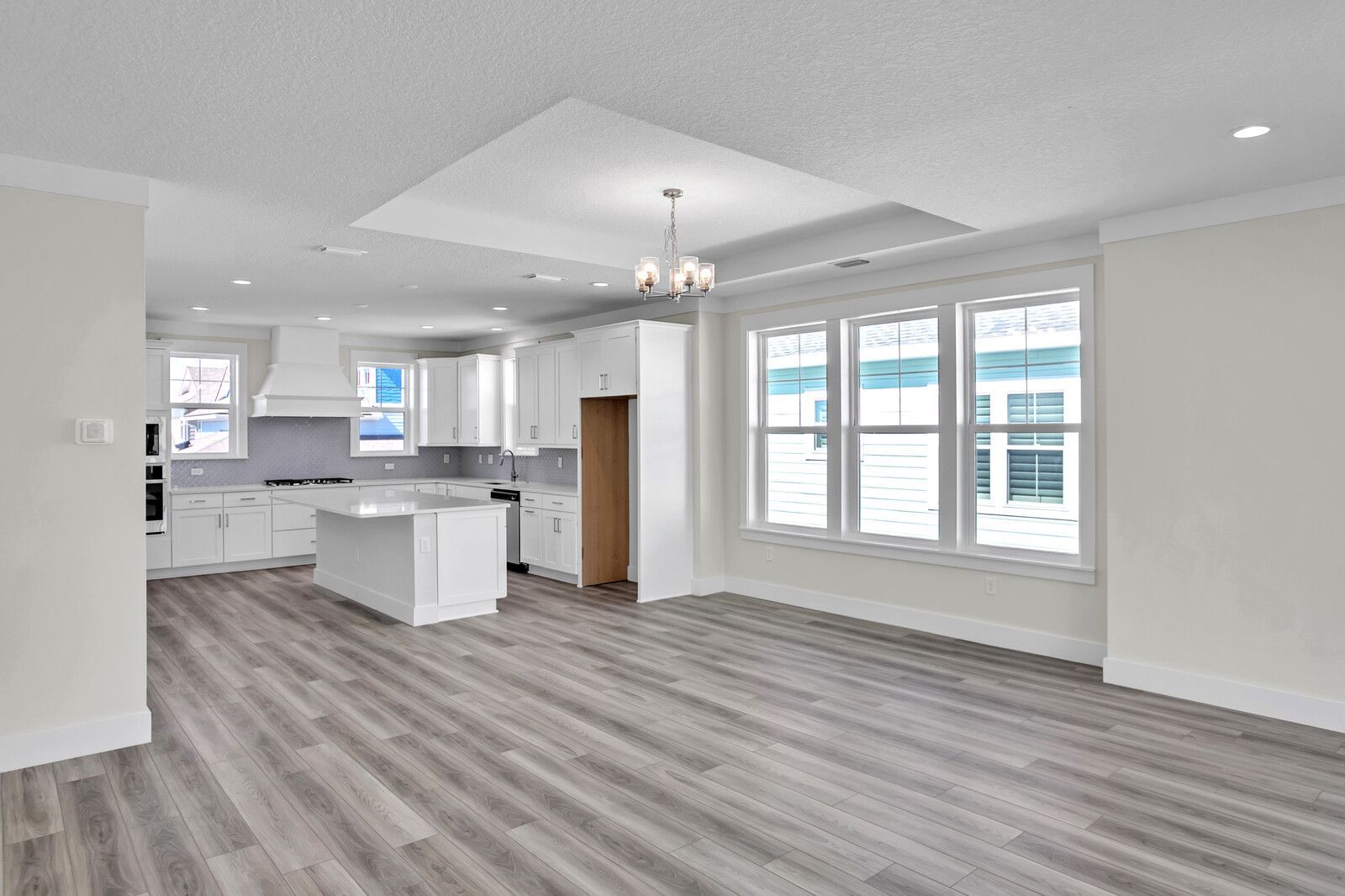 An empty living room with hardwood floors and a kitchen in the background.