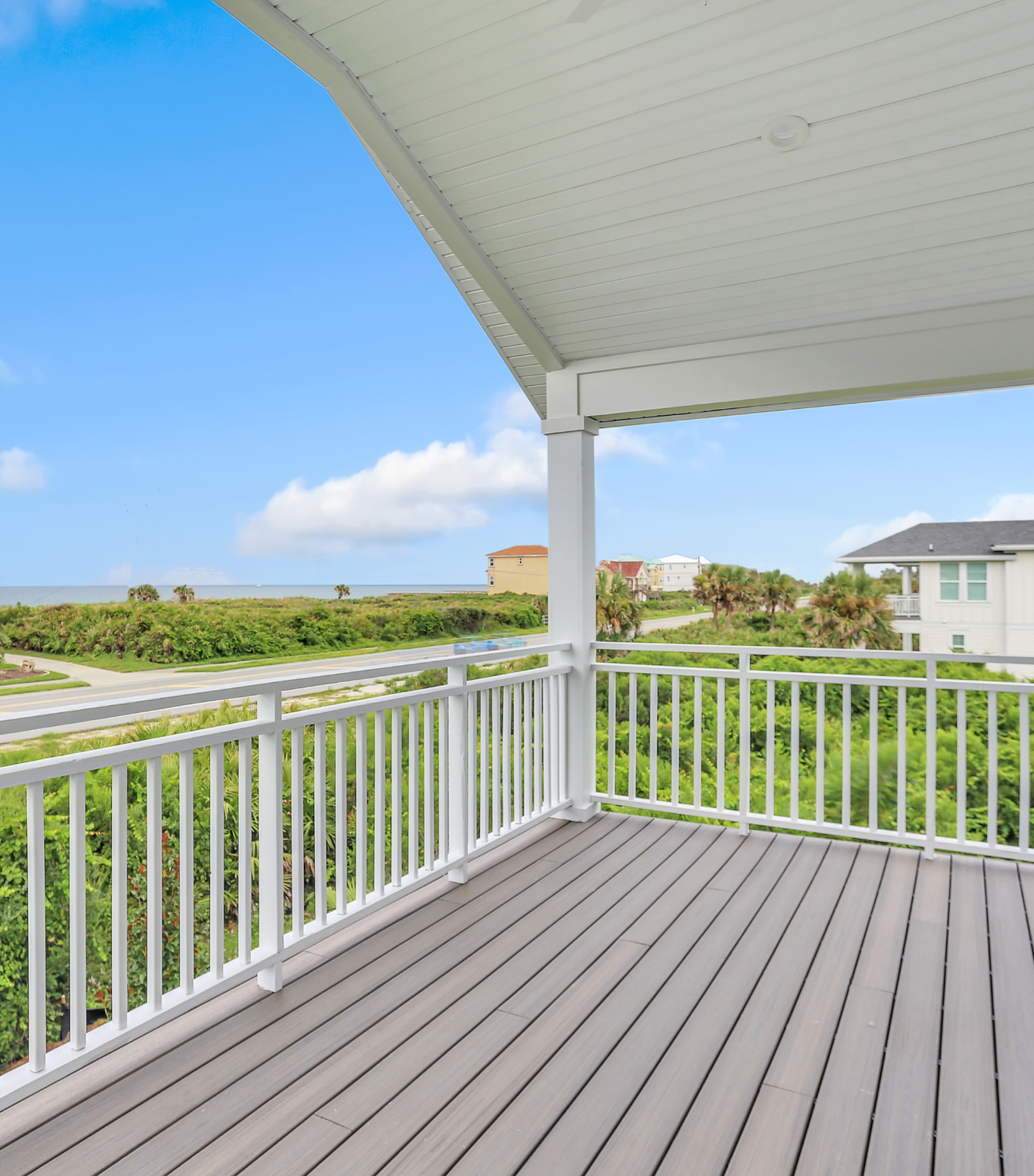 An empty deck with a white railing and a view of the ocean.