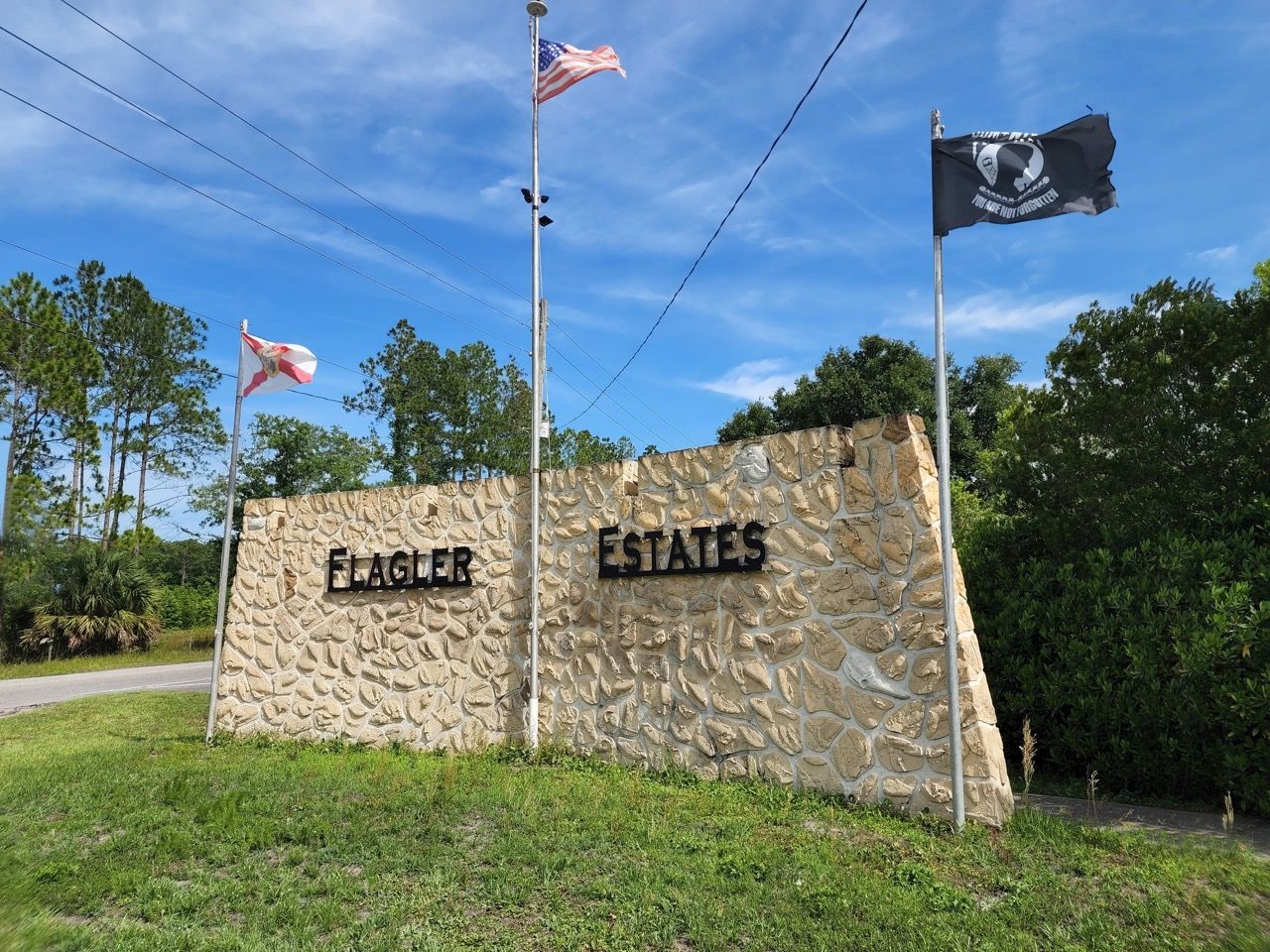 A sign for flagler estates is surrounded by flags