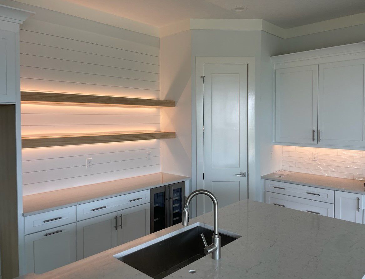 A kitchen with white cabinets , a sink , and a wine cooler.