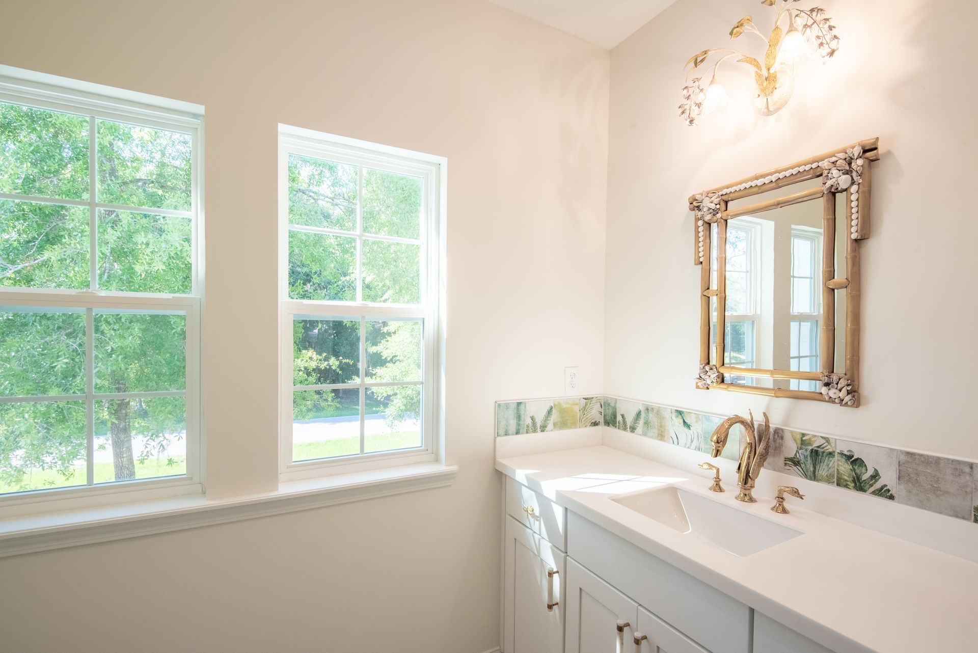 A bathroom with a sink , mirror and two windows.