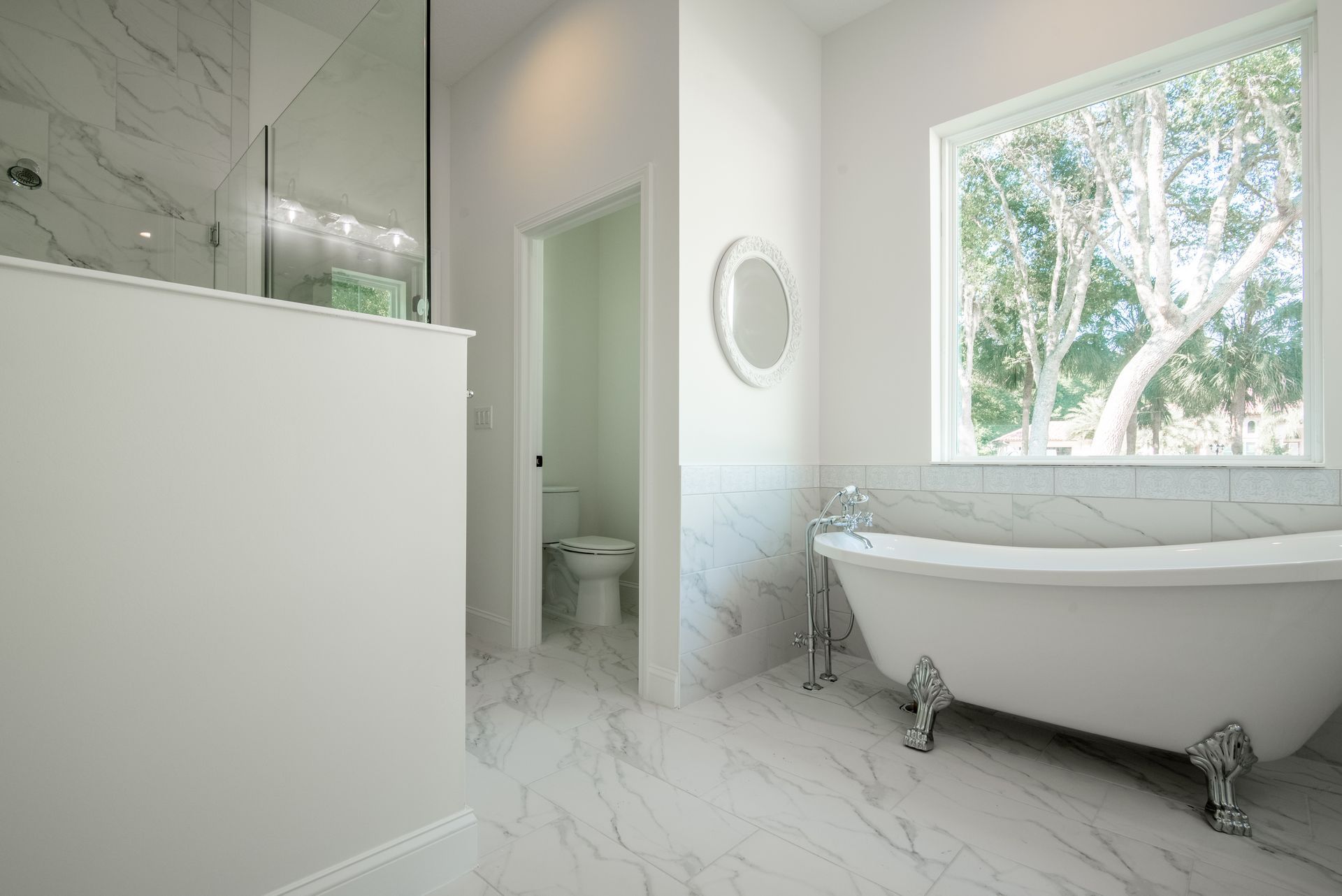 A bathroom with a tub , toilet , mirror and window.