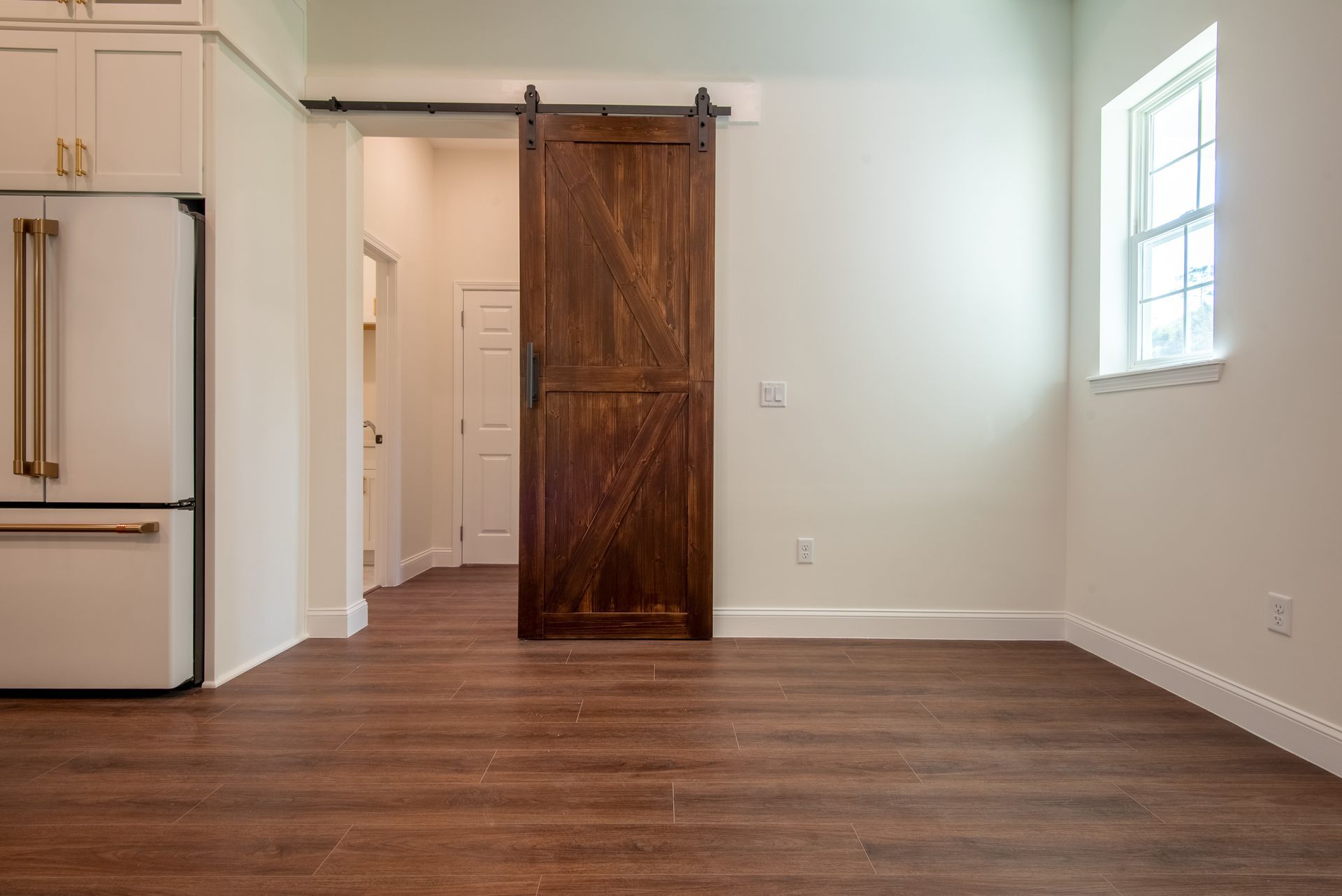 An empty room with a sliding barn door and a refrigerator.