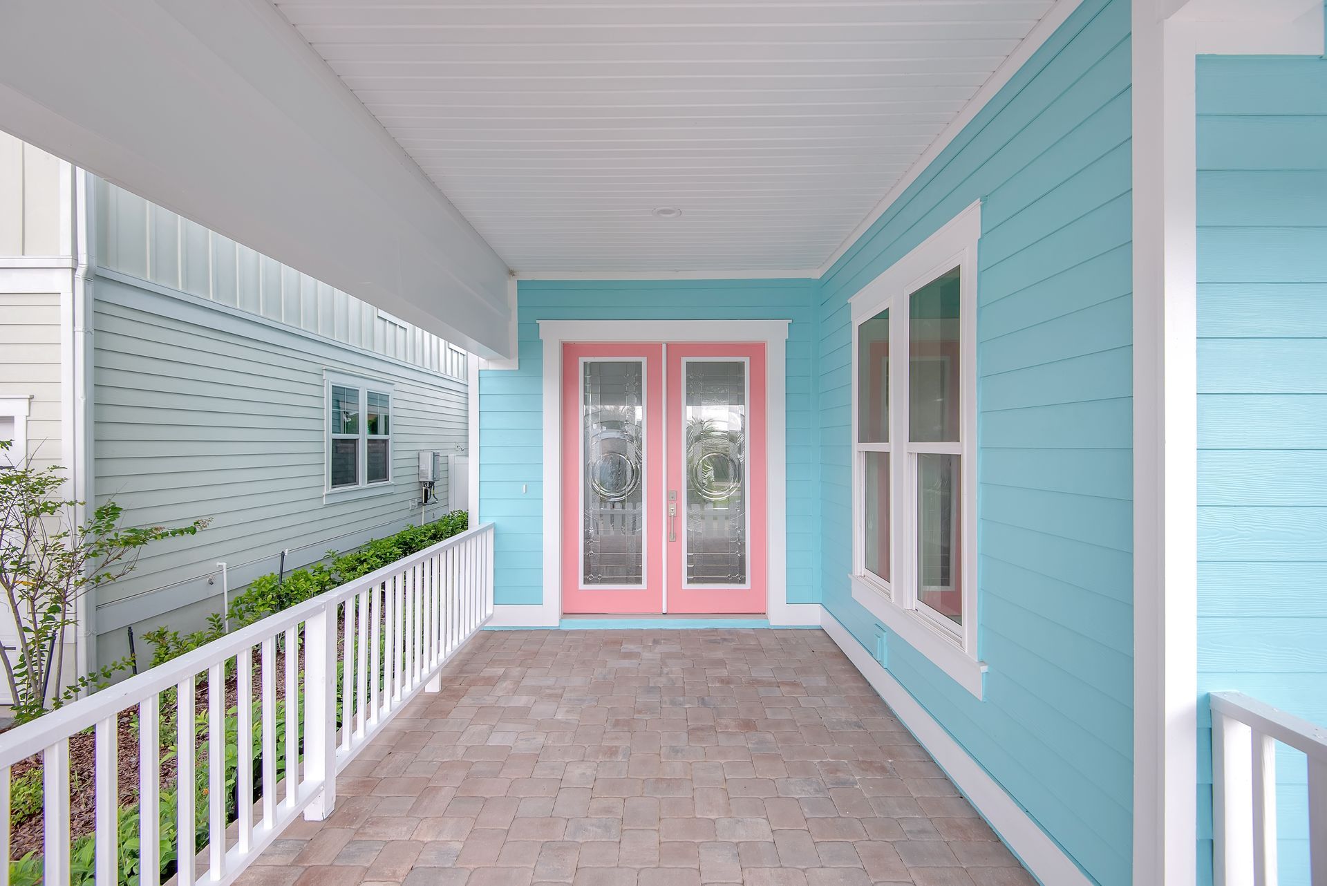A blue house with a pink door and a white railing.