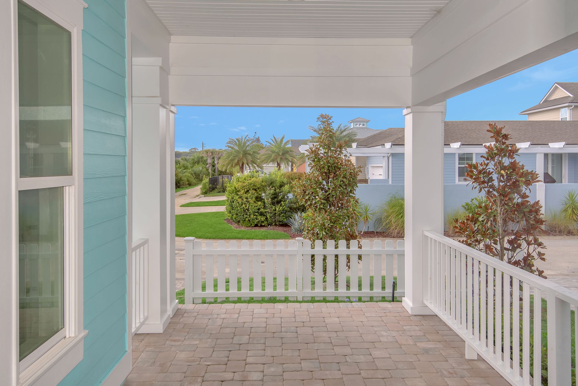 A porch with a white railing and a blue house in the background