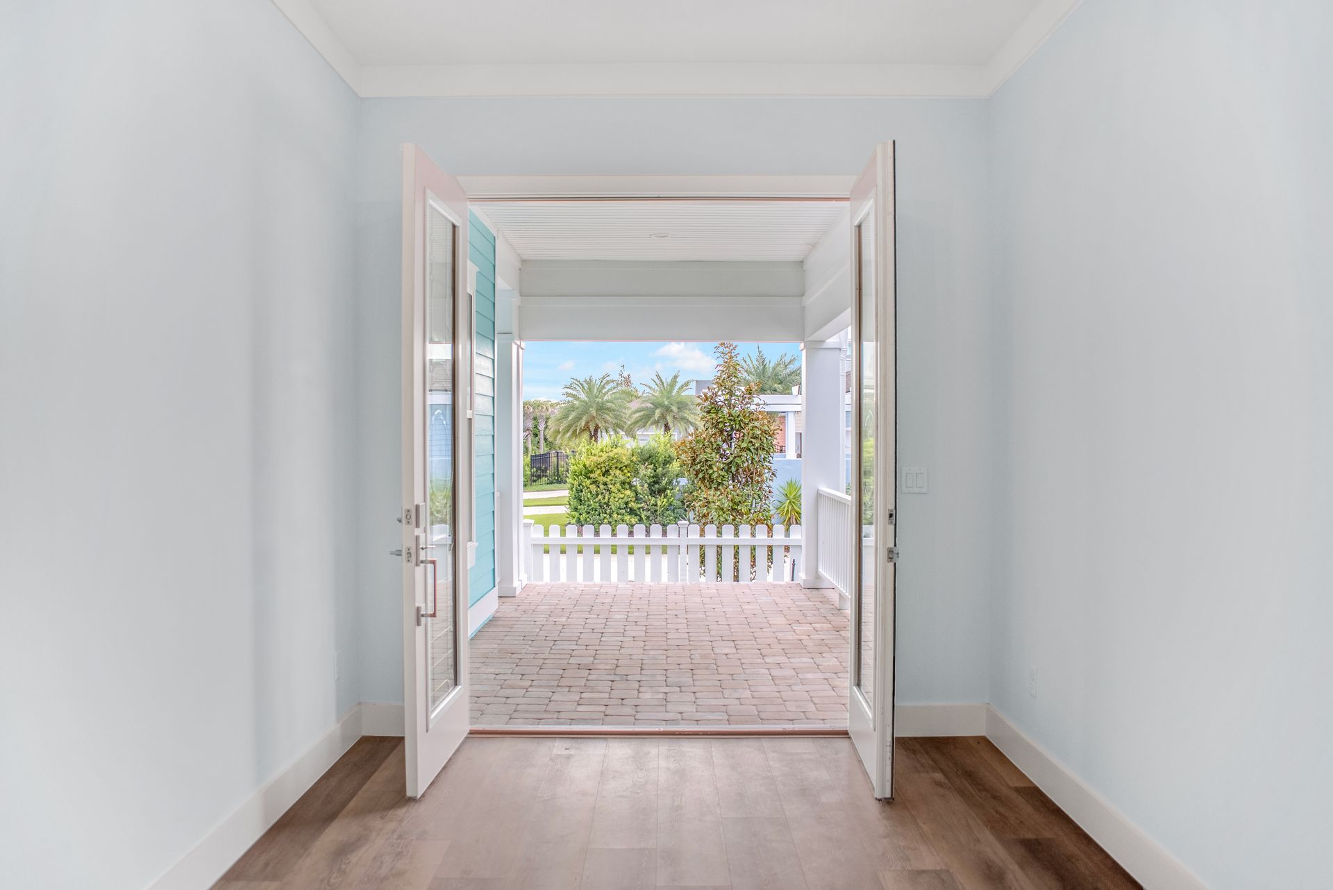 An empty room with a view of a porch and a white picket fence.