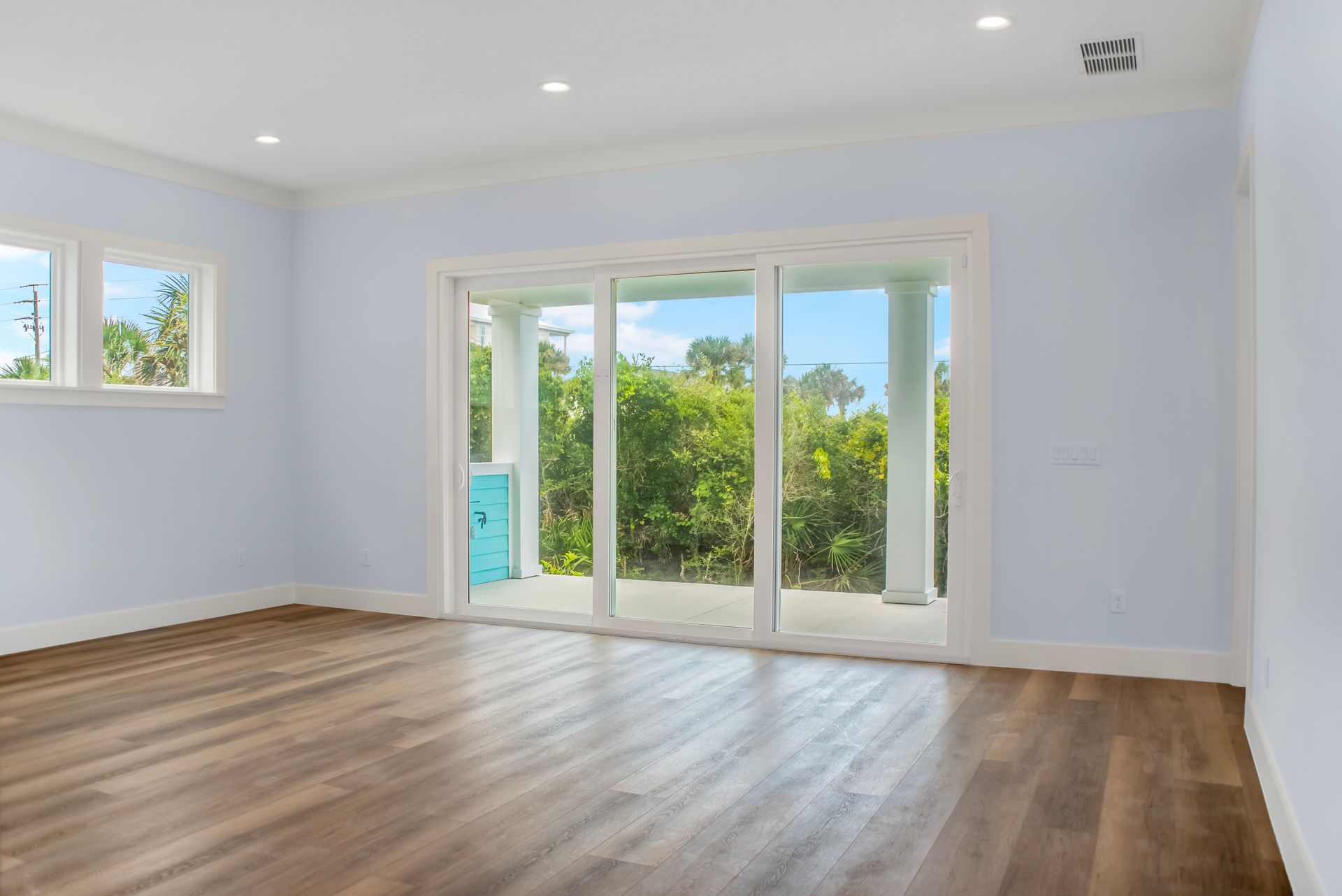 An empty living room with hardwood floors and sliding glass doors.