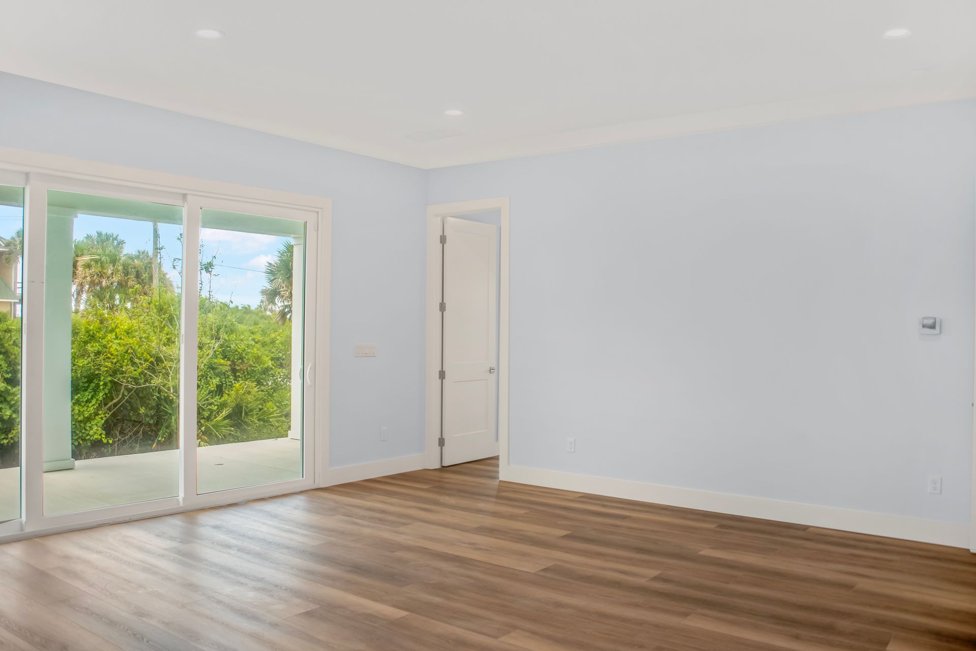 An empty living room with hardwood floors and sliding glass doors.