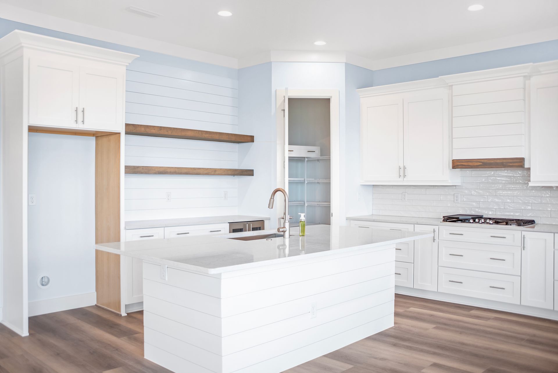 A kitchen with white cabinets , wooden floors , and a large island.