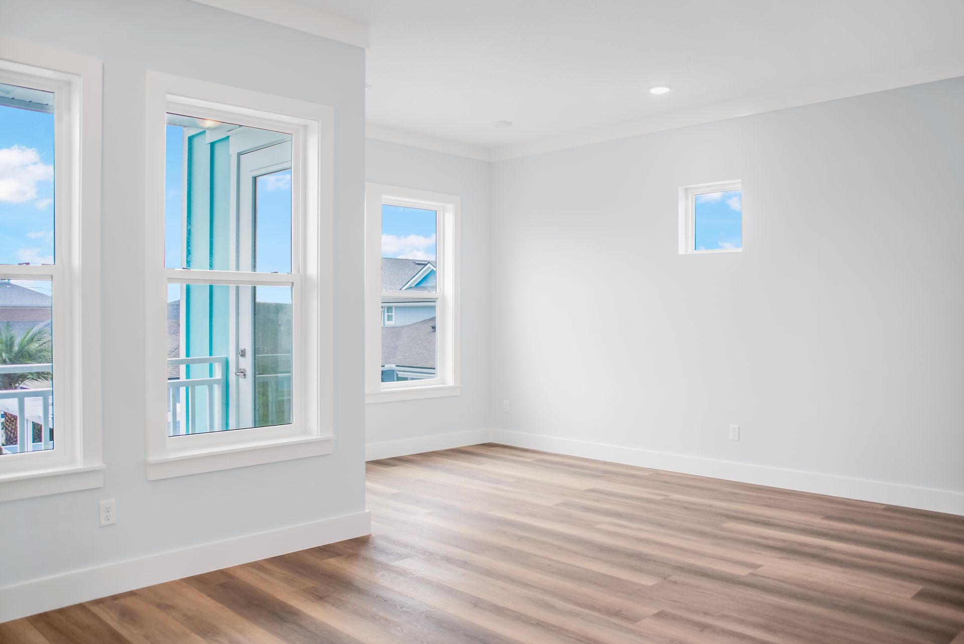 An empty living room with hardwood floors and three windows.