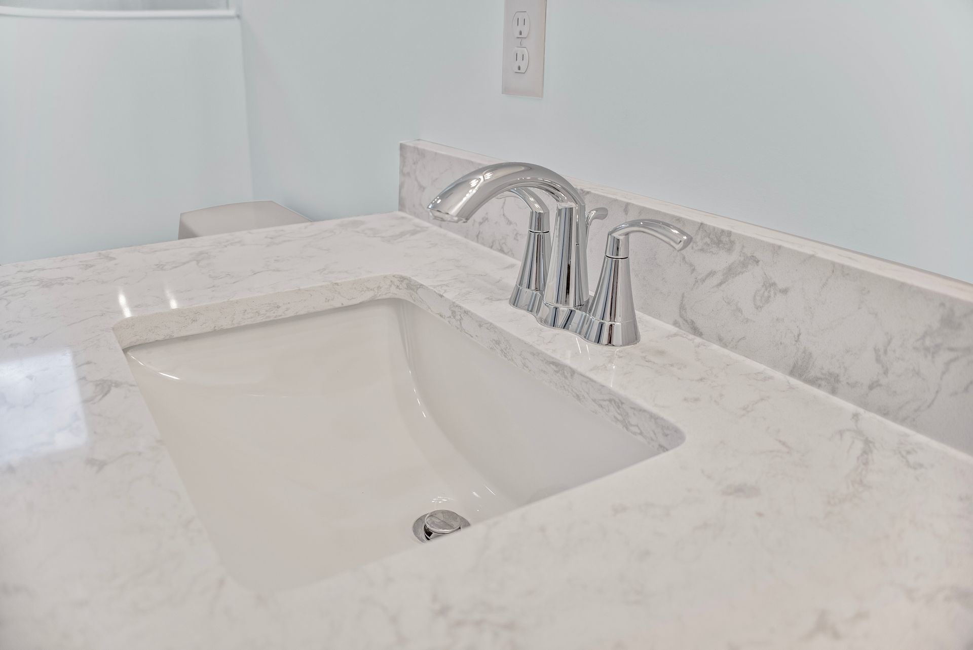 A bathroom sink with a marble counter top and a toilet.