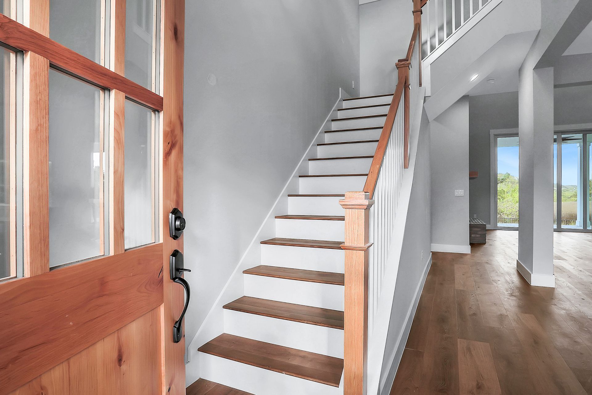 A wooden door is open to a hallway with stairs leading up to the second floor.