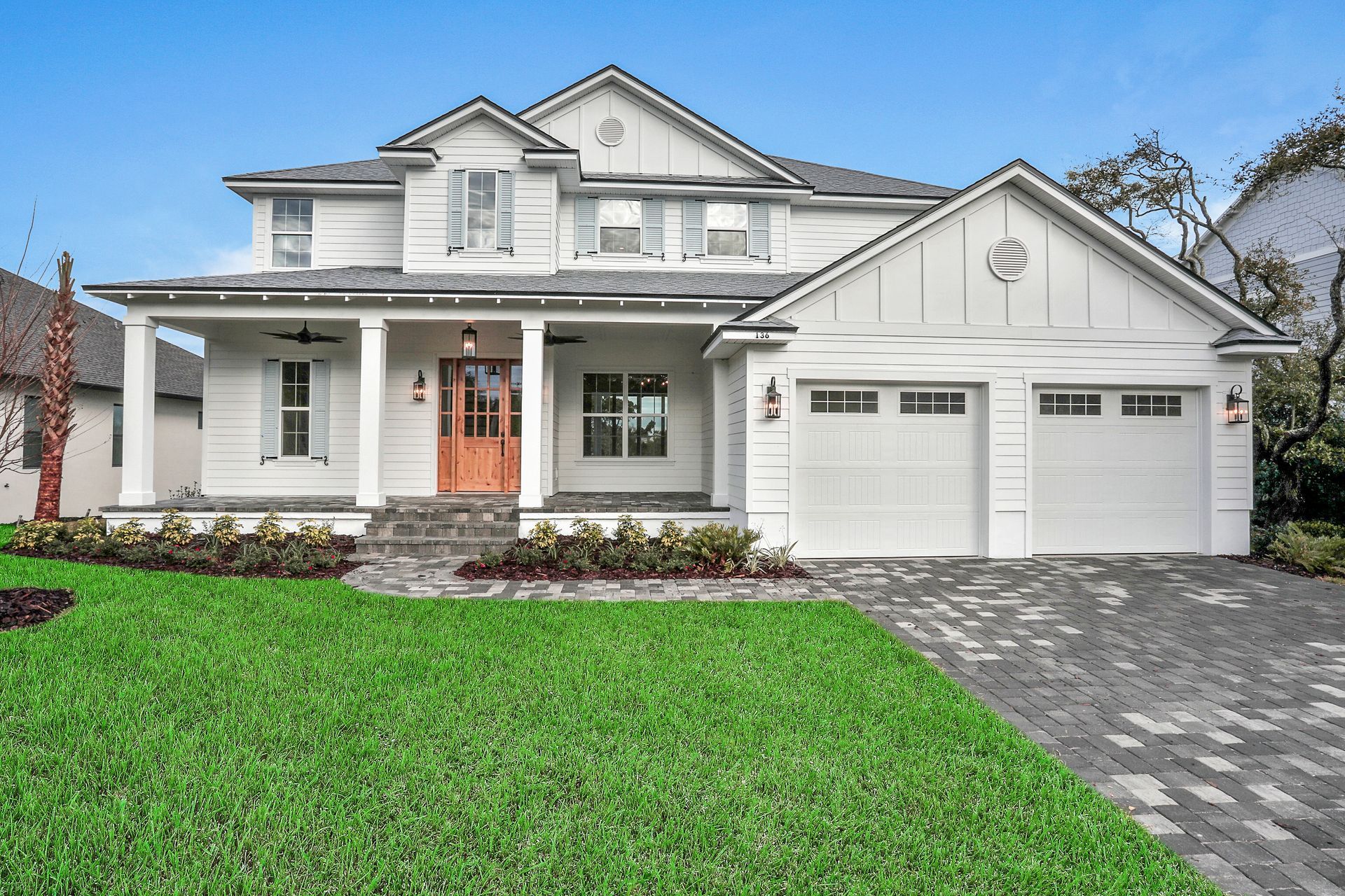 A large white house with two garages and a large lawn in front of it.