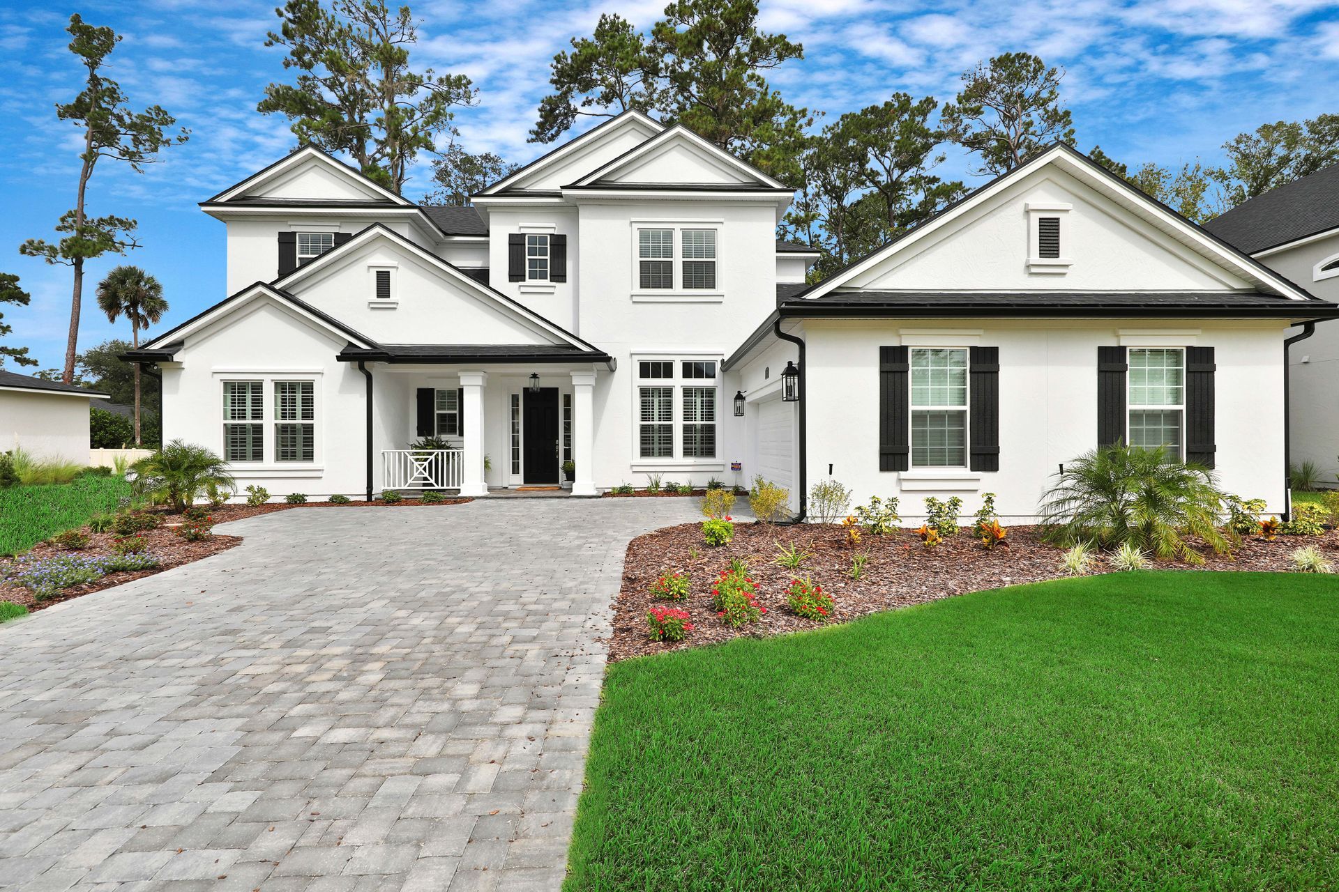 A large white house with black shutters is sitting on top of a lush green lawn.