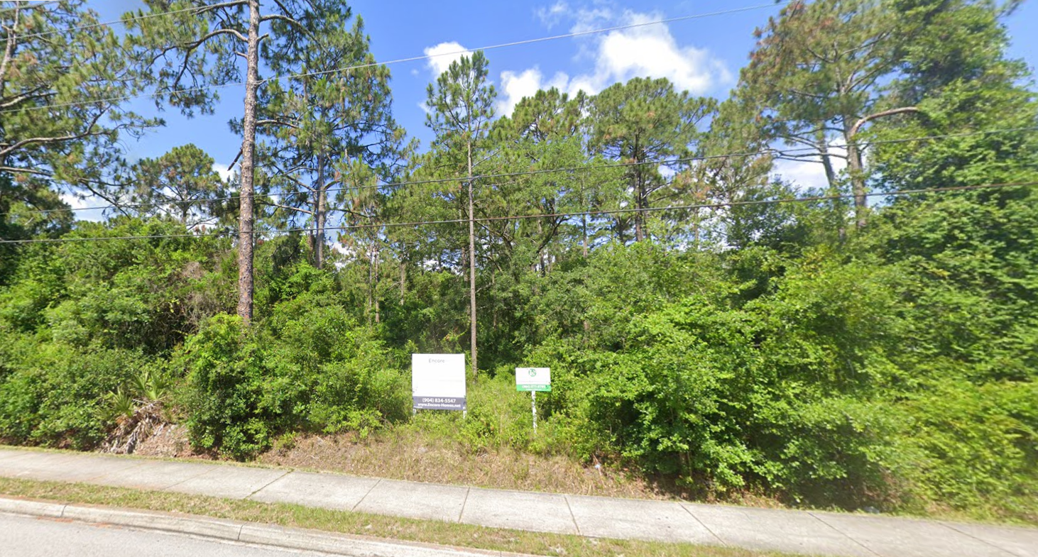 A lot with trees and bushes surrounding it and a road.