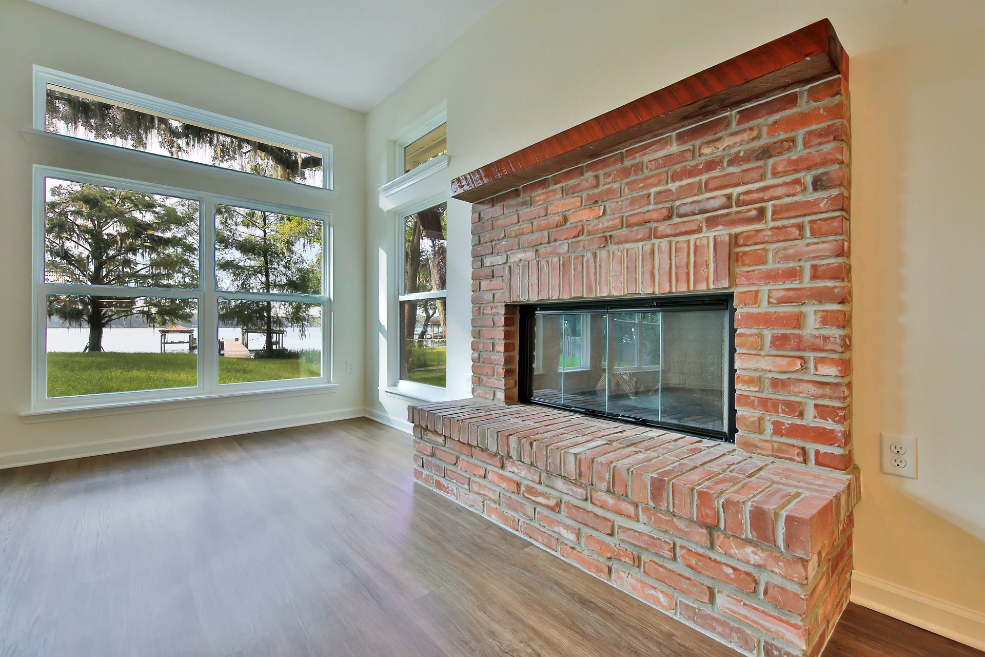 An empty living room with a brick fireplace and lots of windows.