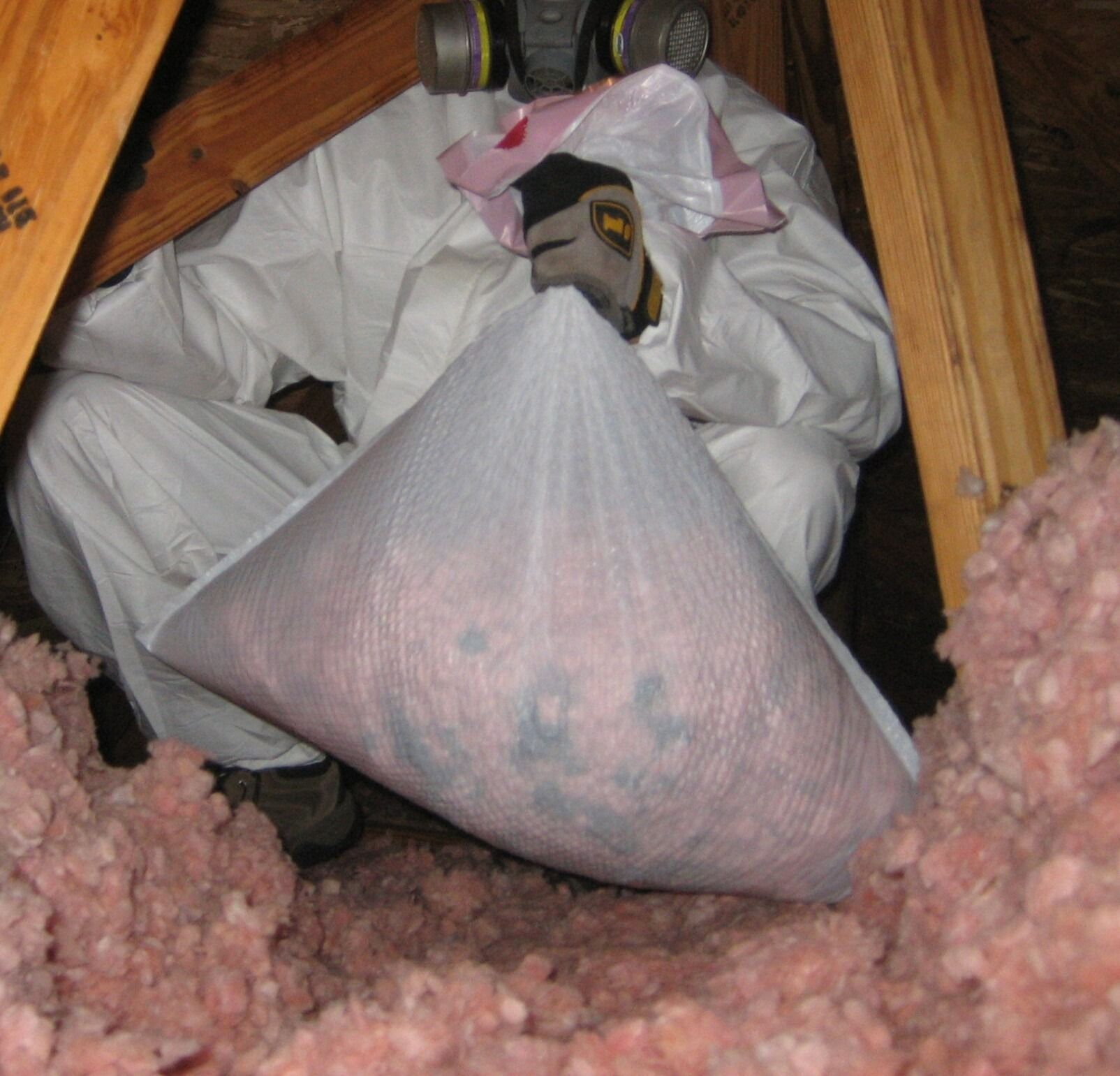 Person in protective suit removing insulation from an attic.