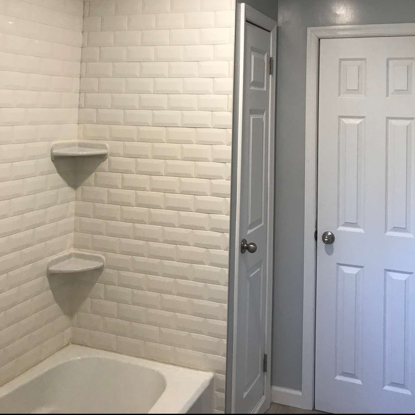 Bathroom with white subway tile shower, corner shelves, and two white doors.