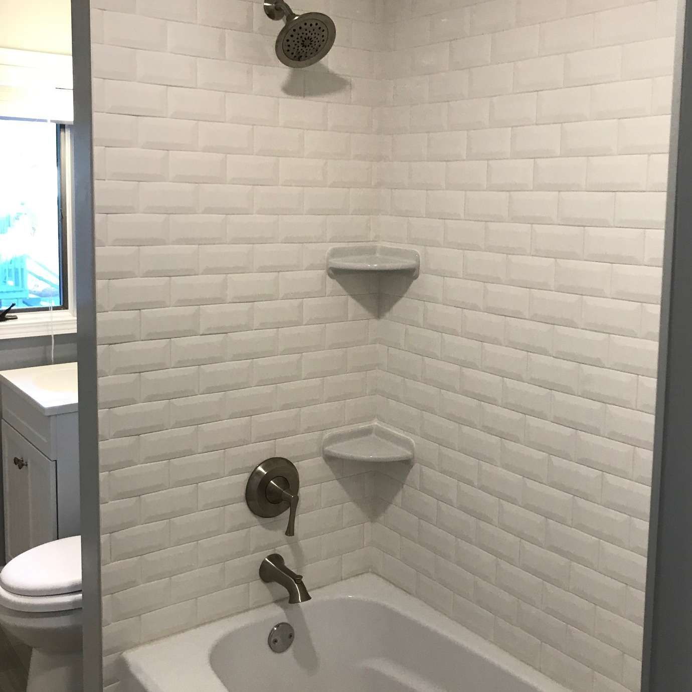 White-tiled shower with a showerhead, two corner shelves, and a bathtub.