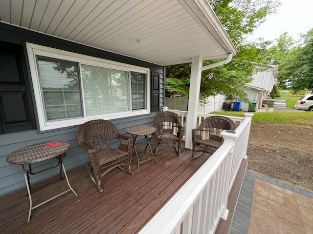 A front porch with brown wicker chairs and tables, under a white awning, next to a sidewalk and lawn.