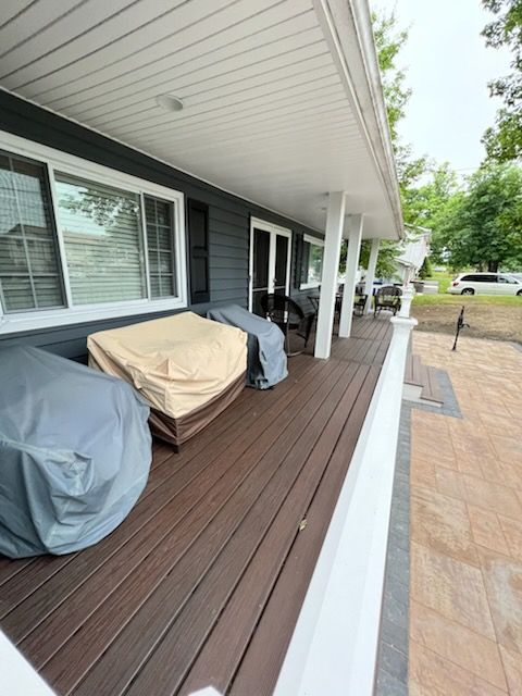 Covered outdoor furniture on a dark wood deck with a white porch roof and columns.