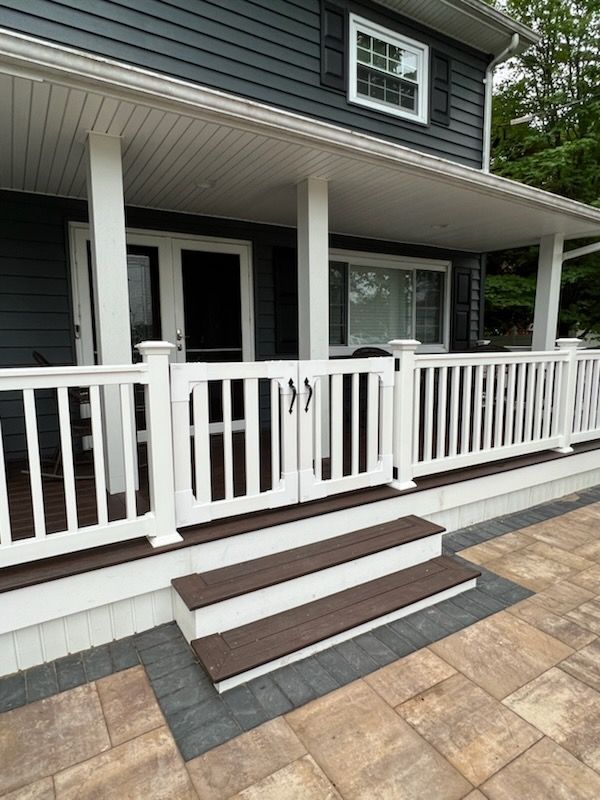 A white fenced porch with steps leading to a house with gray siding and white trim.