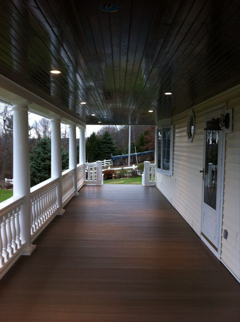 Covered porch with white columns, railing, and dark wooden ceiling and floor. 