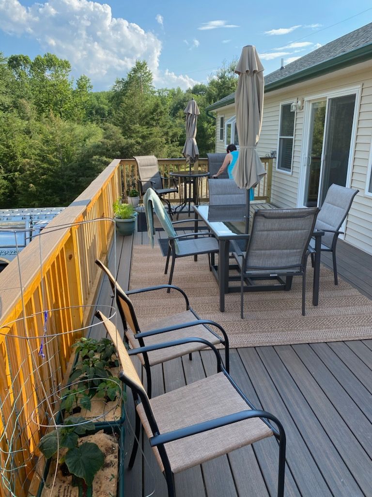 Deck with patio furniture, tan umbrella, and person.