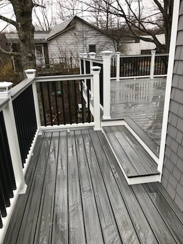 Gray composite deck with black railing and white posts on a cloudy day.