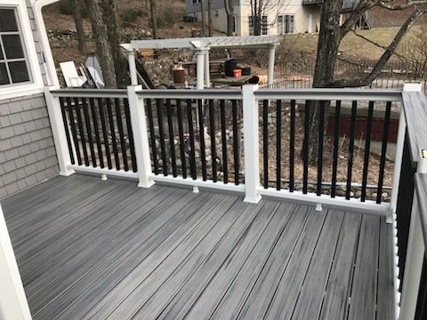 Gray deck with black railing and white posts, overlooking a backyard with trees and a pergola.