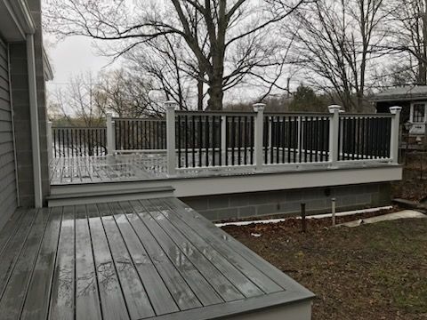 Gray wooden deck with dark railing, overlooking bare trees and a yard.
