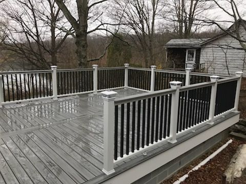 Gray wooden deck with black and white railing, overlooking trees and a shed on a cloudy day.