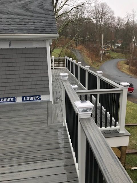 Gray deck with black and white railing overlooking a road and trees.
