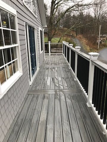 Gray wooden deck with black railings and white posts attached to a gray house.