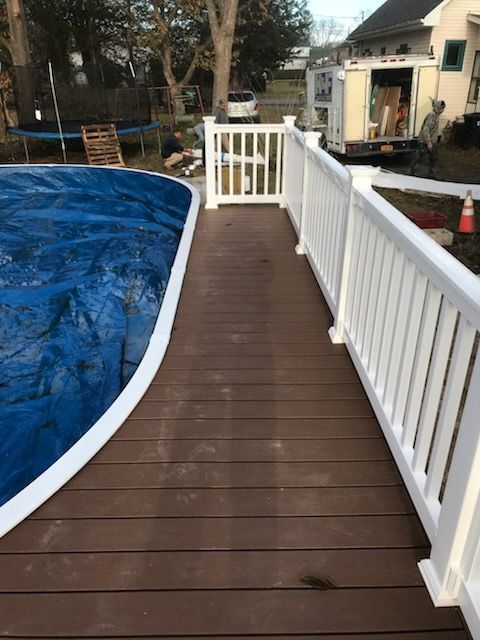 Deck with white railing and gate next to a pool covered with a blue tarp.