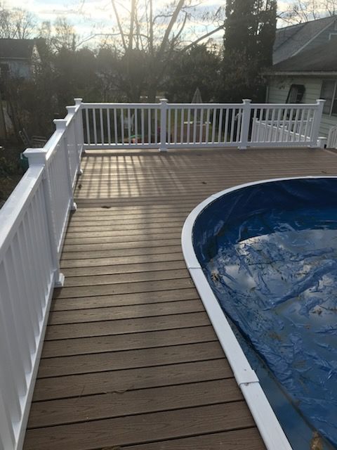 Wooden deck with white railing surrounding a pool with a blue cover.