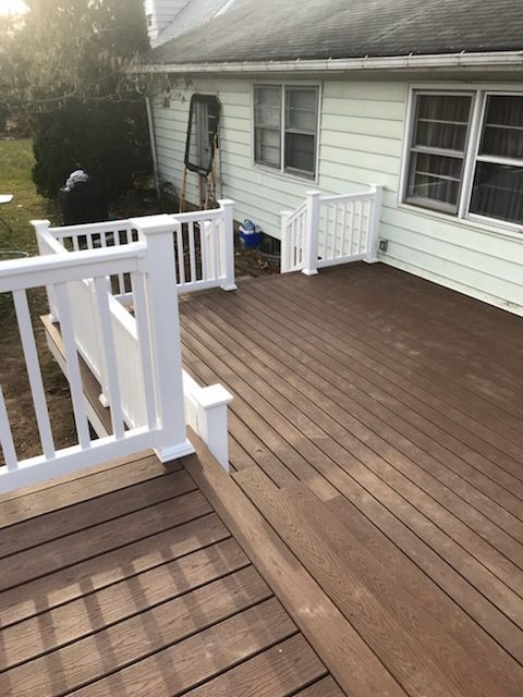 Brown composite deck with white railing, next to a pale green house.