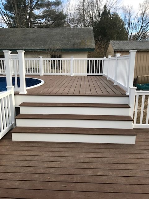 Brown and white deck with steps leading to a raised platform, overlooking a blue pool.