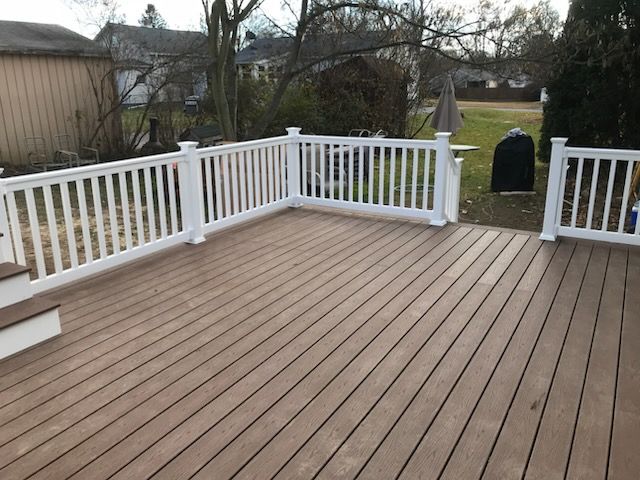 A wooden deck with white railing in a backyard setting.