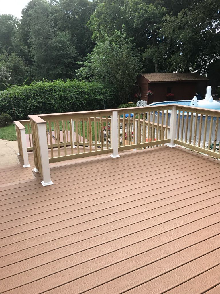 Wooden deck with railing overlooking a swimming pool and trees.