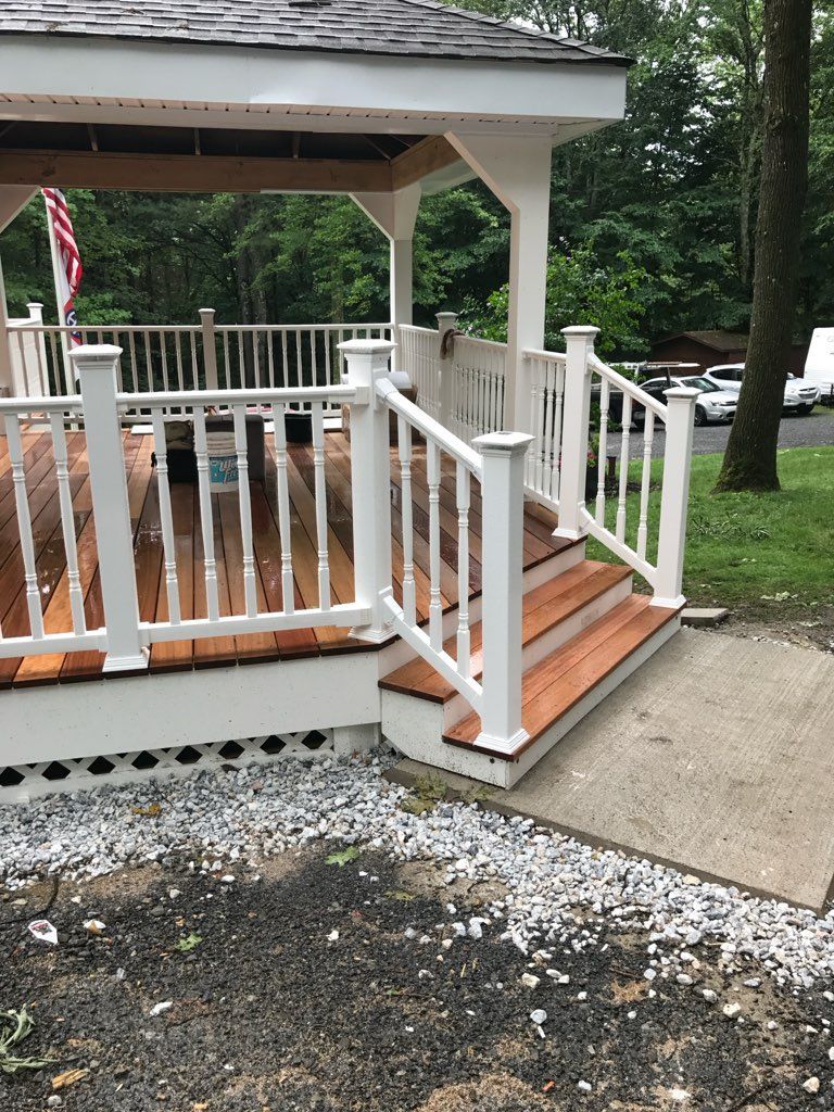 White-railed wooden deck with stairs and a ramp, leading to a gazebo; gravel ground.